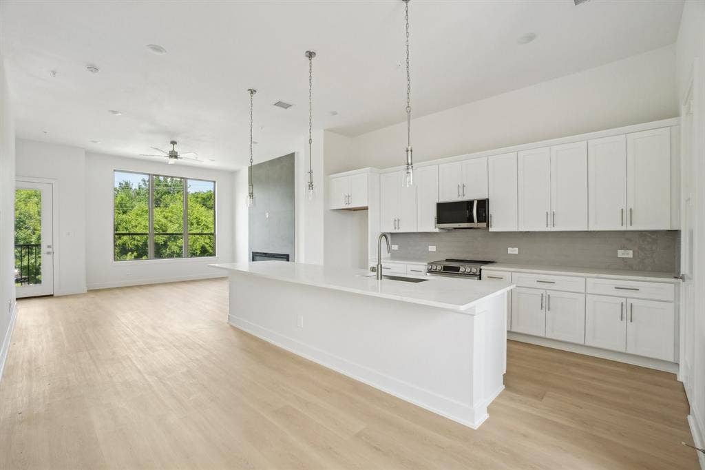 2524 Havenhurst Street, #102, Farmers Branch, TX 75234 Kitchen featuring pendant lighting, white cabinets, a kitchen island with sink, backsplash, and stainless steel appliances
