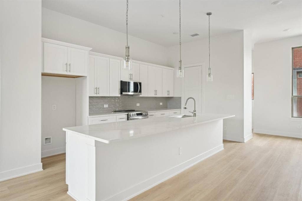 2524 Havenhurst Street, #102, Farmers Branch, TX 75234 Kitchen with hanging light fixtures, white cabinets, an island with sink, appliances with stainless steel finishes, and light wood finished floors