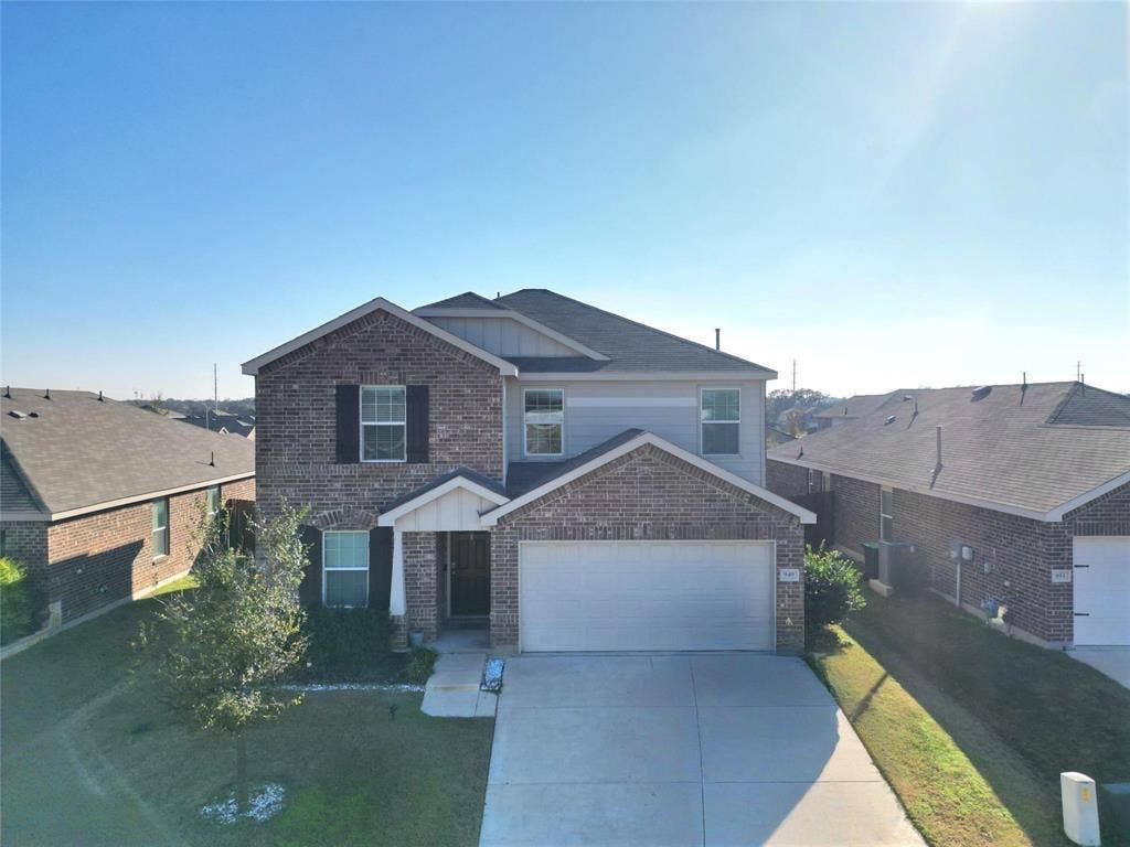 View of front facade featuring a front yard, brick siding, driveway, and an attached garage