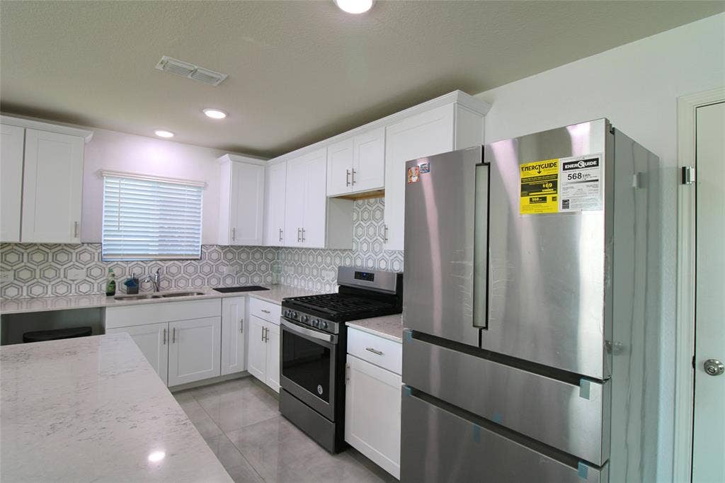 Kitchen featuring appliances with stainless steel finishes, white cabinets, light stone counters, and recessed lighting