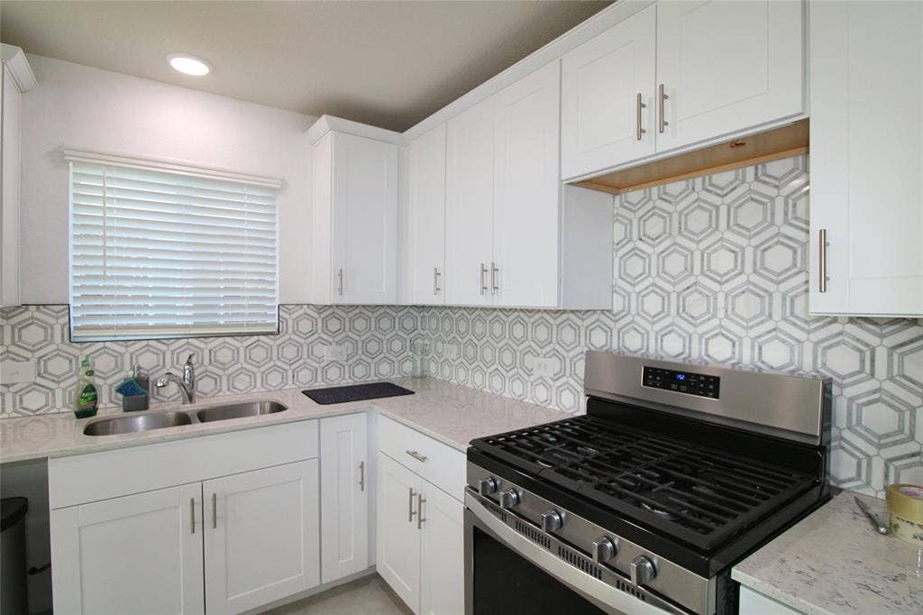 Kitchen with stainless steel range with gas cooktop, light stone countertops, white cabinetry, decorative backsplash, and recessed lighting
