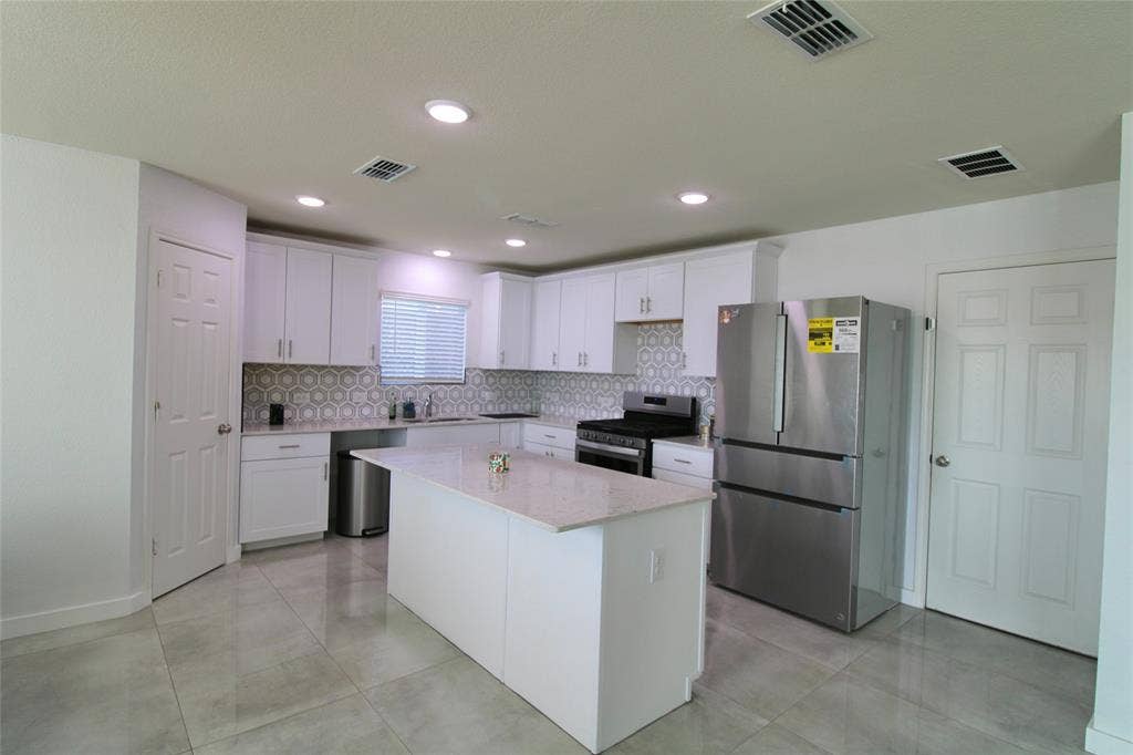Kitchen with stainless steel appliances, white cabinetry, a center island, light stone countertops, and tasteful backsplash