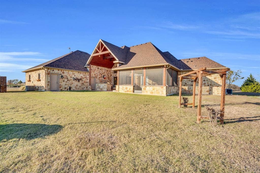 217 Hunter Pass, Waxahachie, TX 75165 View of front facade featuring stone siding, a front yard, roof with shingles, and a sunroom