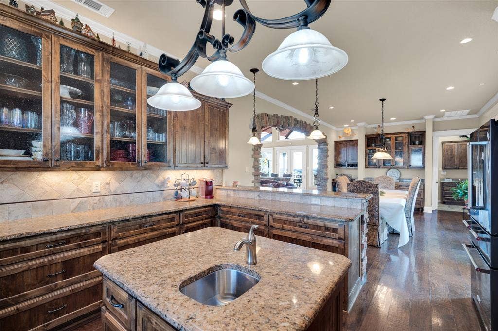 217 Hunter Pass, Waxahachie, TX 75165 Kitchen with glass insert cabinets, open floor plan, ornamental molding, tasteful backsplash, and light stone countertops