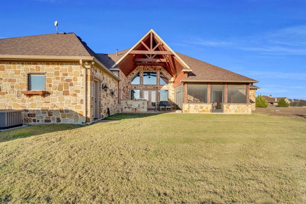 217 Hunter Pass, Waxahachie, TX 75165 Back of house featuring stone siding, a shingled roof, a yard, a patio, and a sunroom