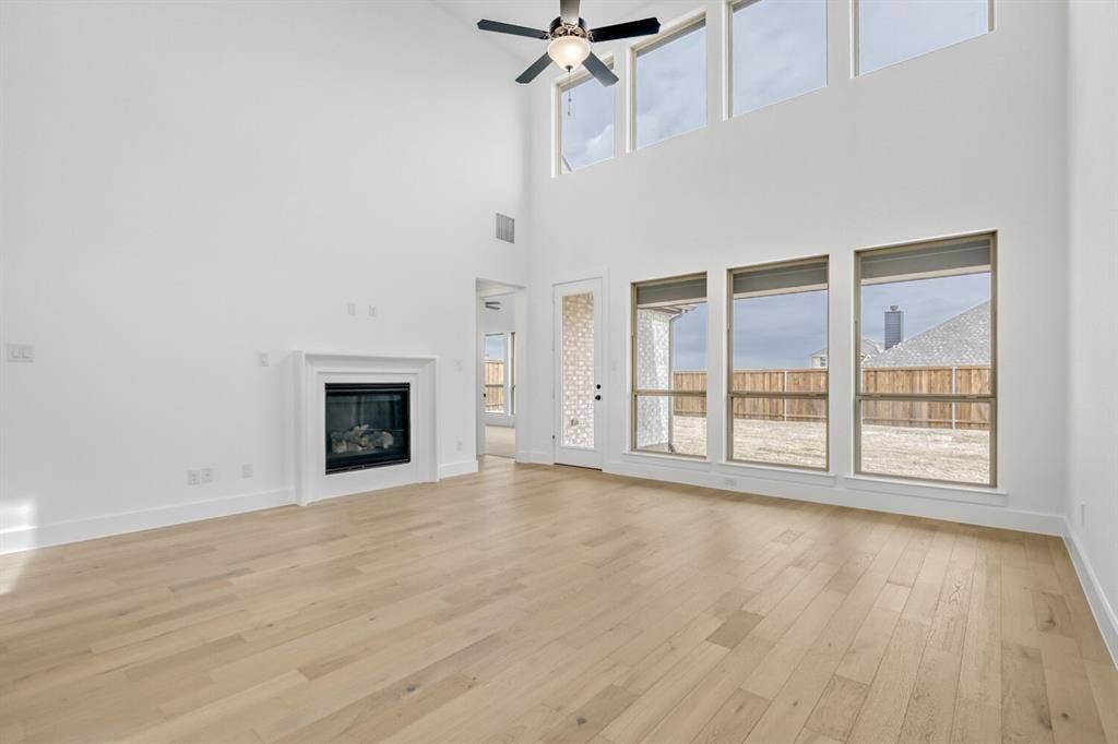 2228 Prickly Cactus Drive, Forney, TX 75126 Unfurnished living room with a glass covered fireplace, a ceiling fan, light wood finished floors, and a high ceiling