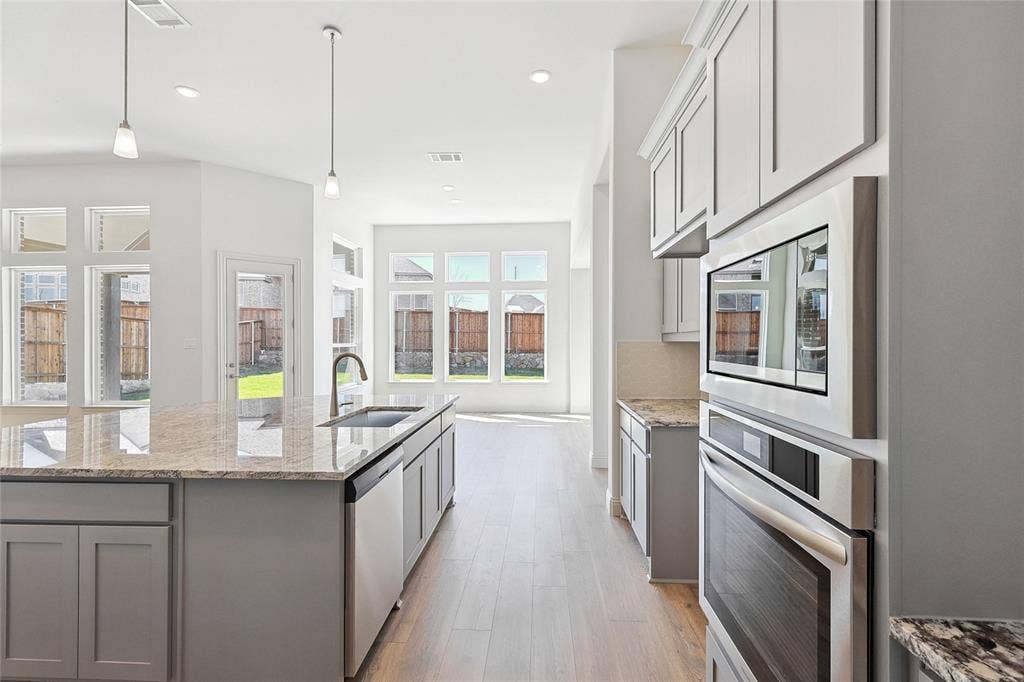 313 Trinity Court, Shady Shores, TX 76208 Kitchen with appliances with stainless steel finishes, light stone countertops, light wood finished floors, a center island with sink, and recessed lighting