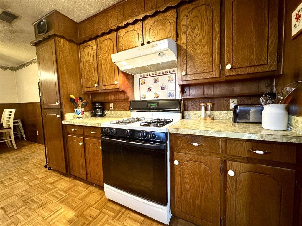 317 N Trail Street, Crowley, TX 76036 Kitchen featuring white range with gas cooktop, under cabinet range hood, light countertops, a textured ceiling, and wooden walls