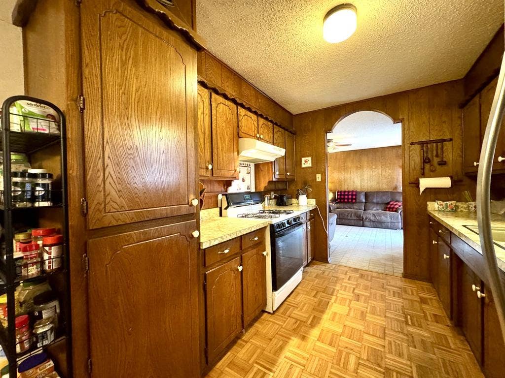 317 N Trail Street, Crowley, TX 76036 Kitchen featuring arched walkways, white range with gas stovetop, light countertops, a textured ceiling, and under cabinet range hood