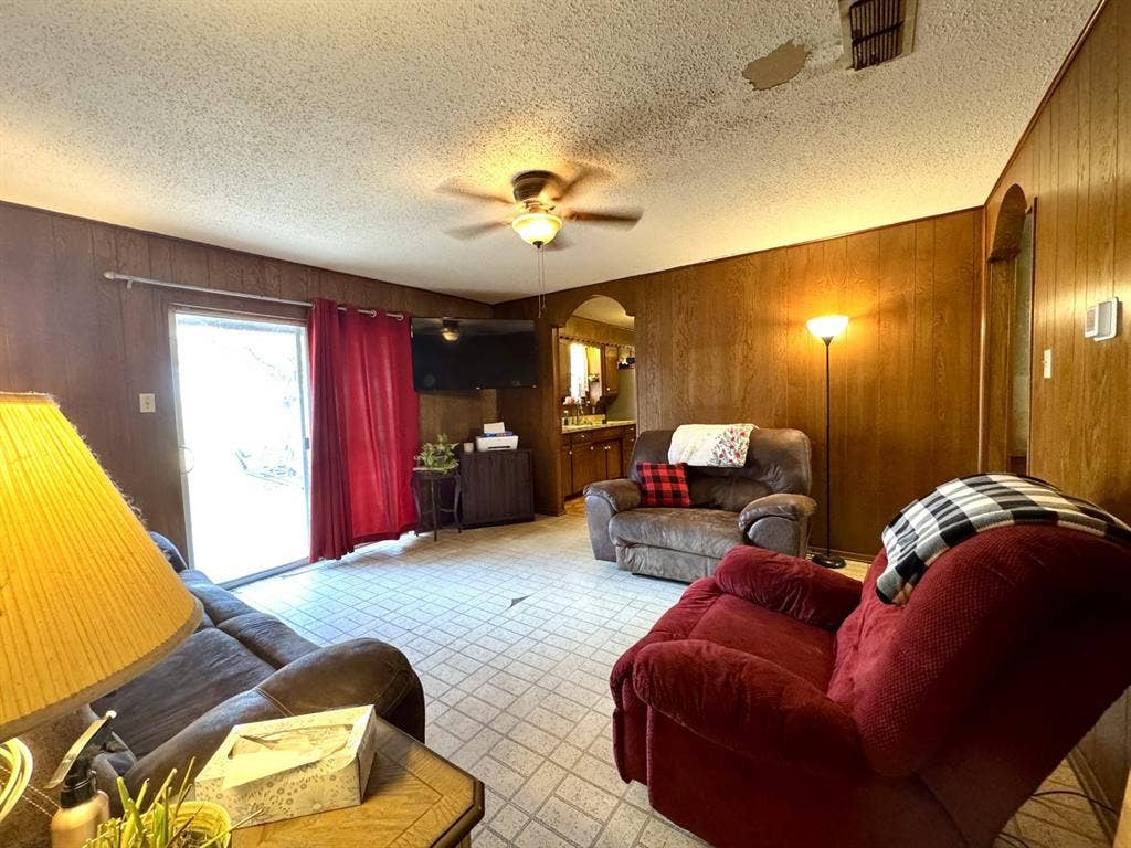 317 N Trail Street, Crowley, TX 76036 Living area with arched walkways, wood walls, a ceiling fan, and a textured ceiling