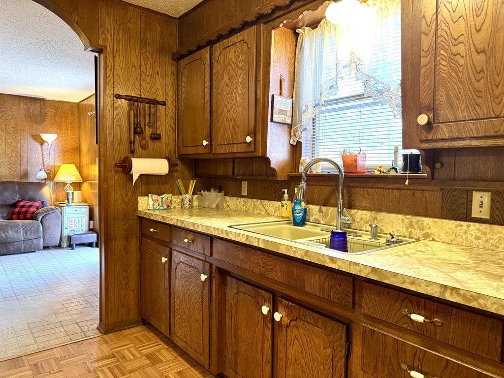 317 N Trail Street, Crowley, TX 76036 Kitchen with wood walls, light countertops, arched walkways, brown cabinets, and a textured ceiling