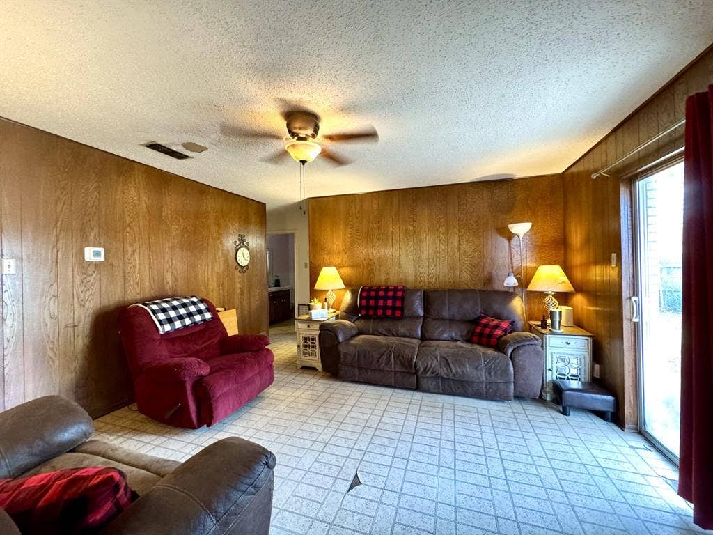 317 N Trail Street, Crowley, TX 76036 Living room featuring wooden walls, a ceiling fan, and a textured ceiling