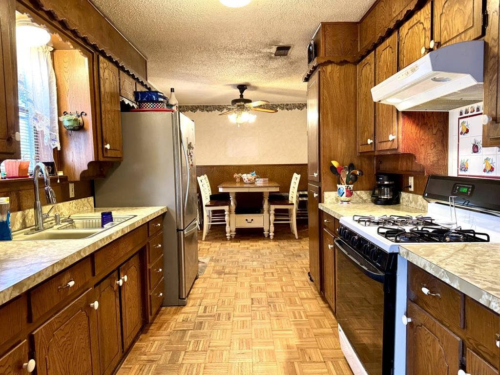 317 N Trail Street, Crowley, TX 76036 Kitchen featuring black range with gas cooktop, a textured ceiling, under cabinet range hood, freestanding refrigerator, and light countertops