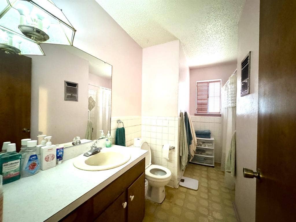 317 N Trail Street, Crowley, TX 76036 Bathroom featuring vanity, a textured ceiling, a shower with curtain, tile walls, and a wainscoted wall