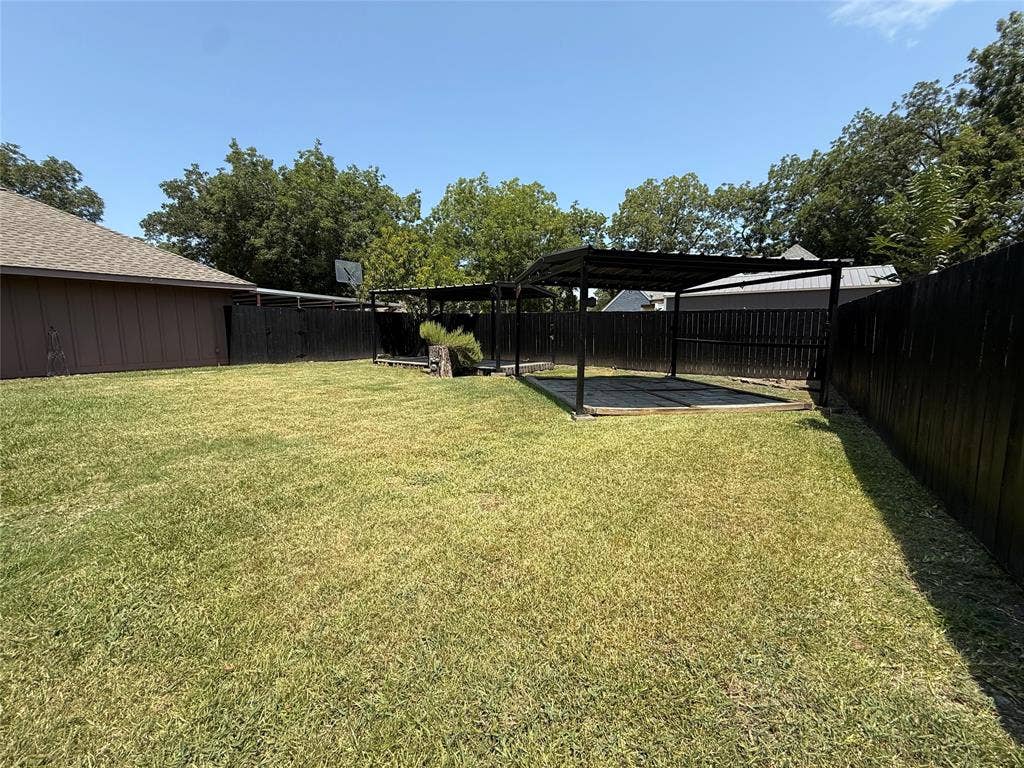6018 Raleigh Drive, Garland, TX 75044 Expansive backyard featuring a large grass area, wood privacy fencing, and a covered patio structure