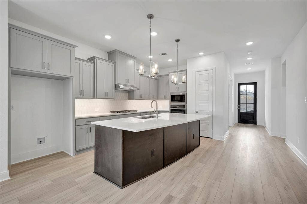 2079 Emerald Grove Lane, Arlington, TX 76005 Kitchen featuring hanging lights, a kitchen island with sink, gray cabinetry, light wood-type flooring, and light stone counters