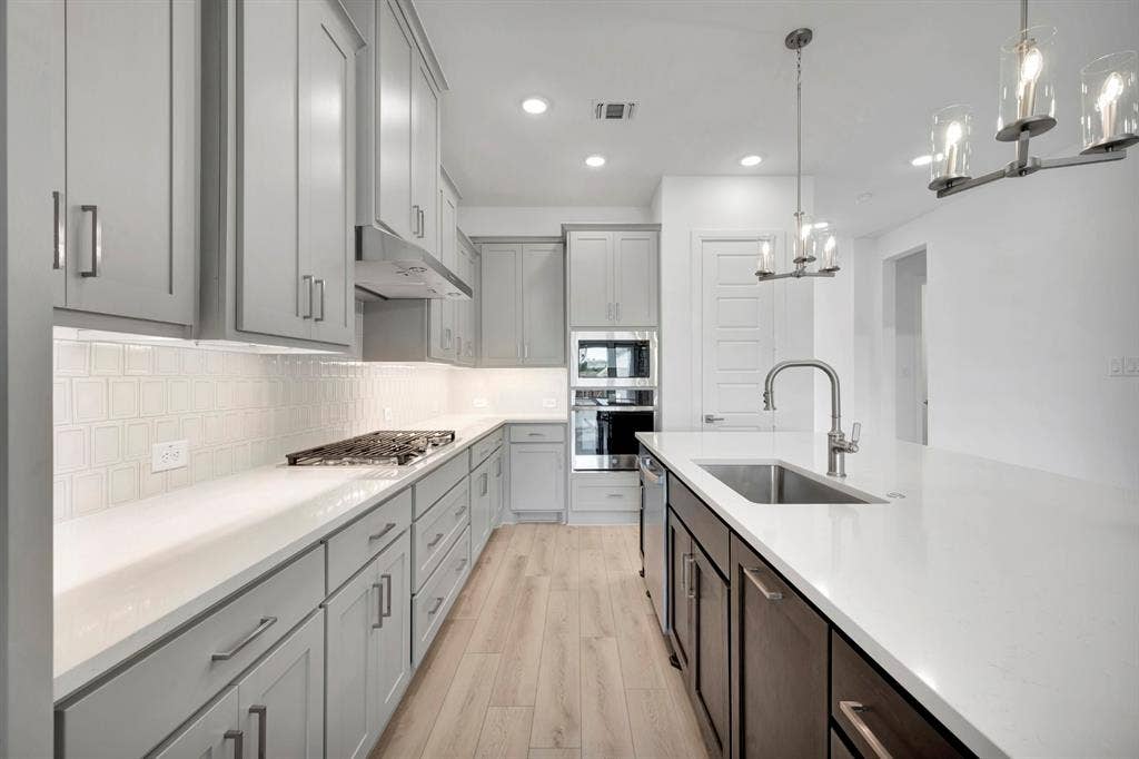 2079 Emerald Grove Lane, Arlington, TX 76005 Kitchen featuring stainless steel appliances, light wood-type flooring, suspended lighting, tasteful backsplash, and light stone counters