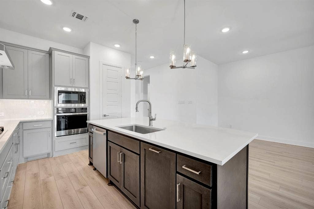 2079 Emerald Grove Lane, Arlington, TX 76005 Kitchen featuring light wood-style floors, stainless steel appliances, an island with sink, suspended lighting, and backsplash