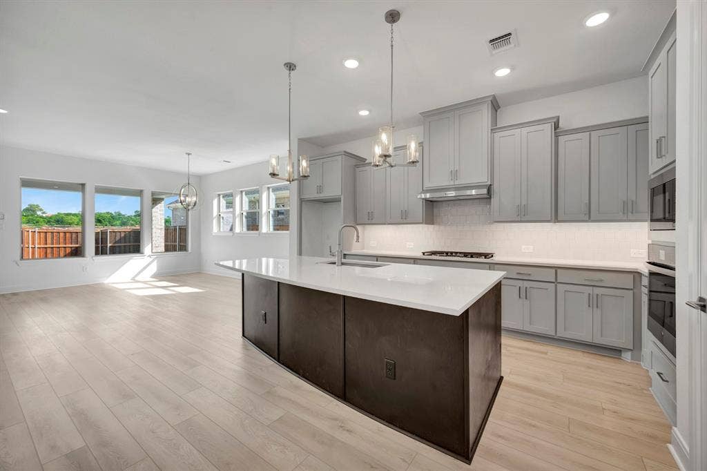 2079 Emerald Grove Lane, Arlington, TX 76005 Kitchen featuring a chandelier, gray cabinetry, a kitchen island with sink, stainless steel appliances, and light wood-style floors