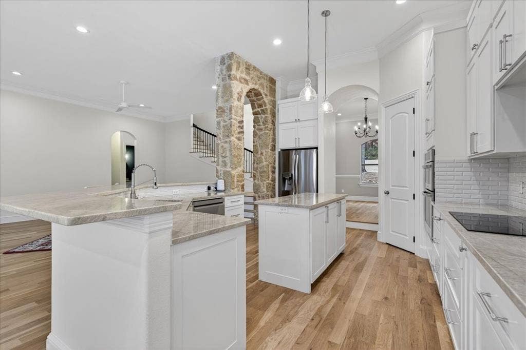 5182 Bayshore Drive, Athens, TX 75752 Kitchen featuring arched walkways, crown molding, light wood-style floors, white cabinetry, and light stone countertops