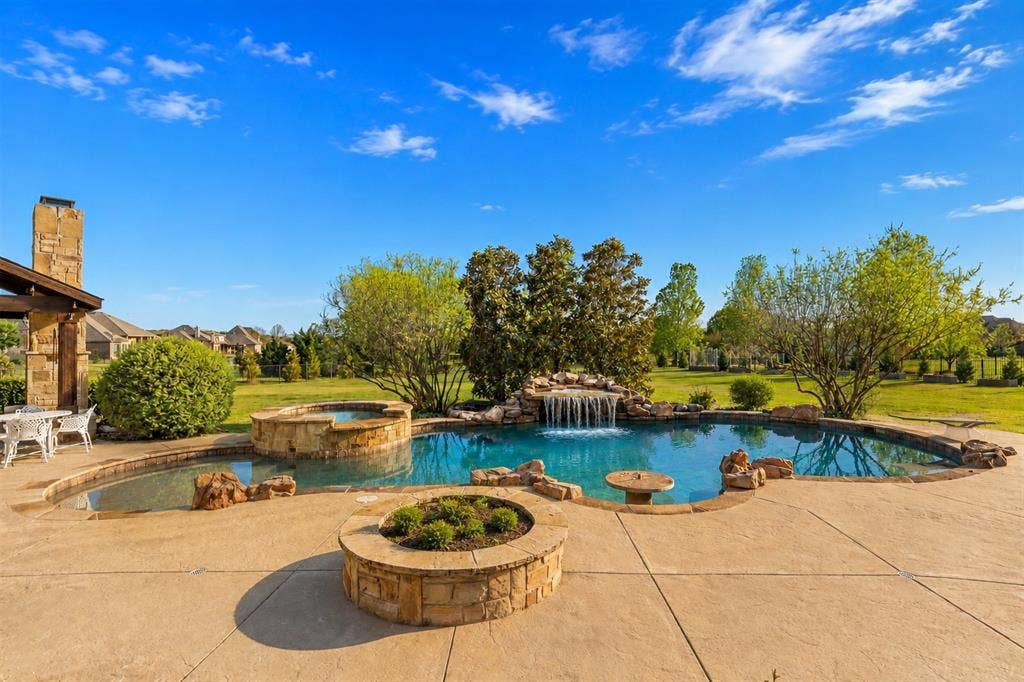 Custom-shaped swimming pool with a stone waterfall feature, integrated hot tub, and surrounding stamped concrete patio