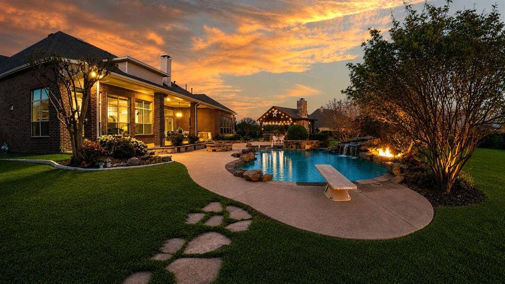 Expansive backyard featuring a freeform swimming pool with a diving board, rock waterfall, and integrated fire feature