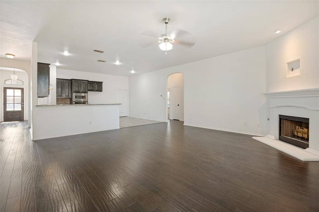 Expansive living area featuring wood-finish flooring, a white mantel fireplace, and a ceiling fan