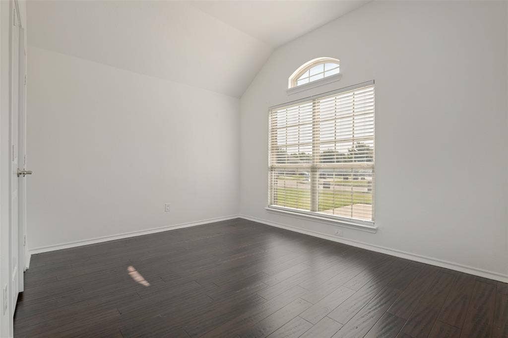 Vaulted ceiling room featuring a large window with blinds and an arched transom window