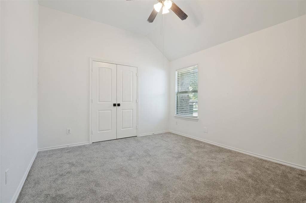 Spacious room featuring vaulted ceilings, light gray carpeting, and a ceiling fan with integrated lighting