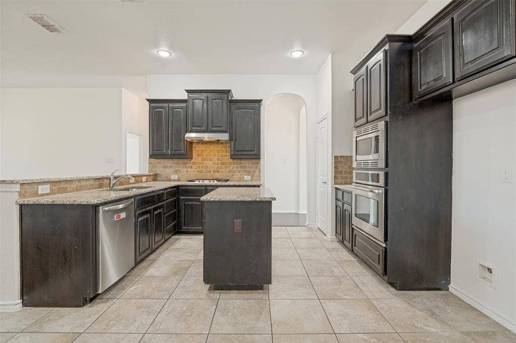Kitchen featuring dark wood cabinetry, light-toned tile flooring, and granite countertops