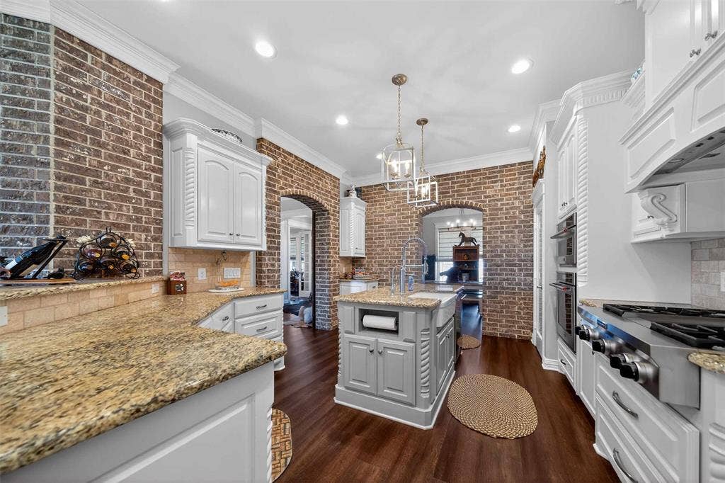 23151 Champion Drive, Lindale, TX 75771 Kitchen with crown molding, arched walkways, dark wood-style flooring, a kitchen island with sink, and light stone countertops