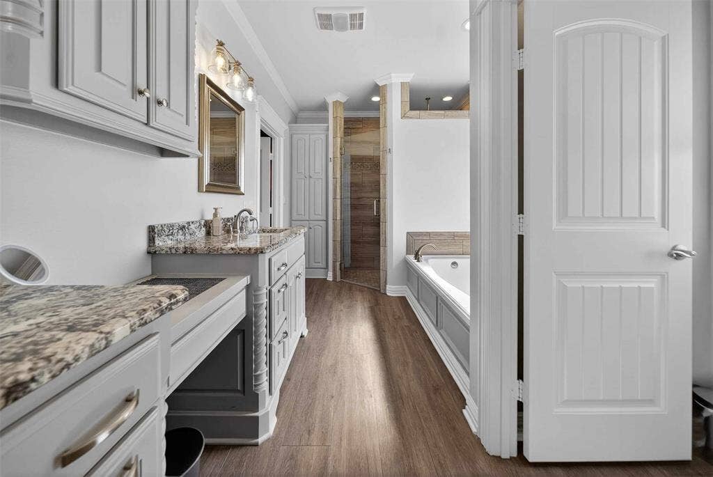 23151 Champion Drive, Lindale, TX 75771 Full bathroom featuring two vanities, a stall shower, a garden tub, ornamental molding, and dark wood-type flooring