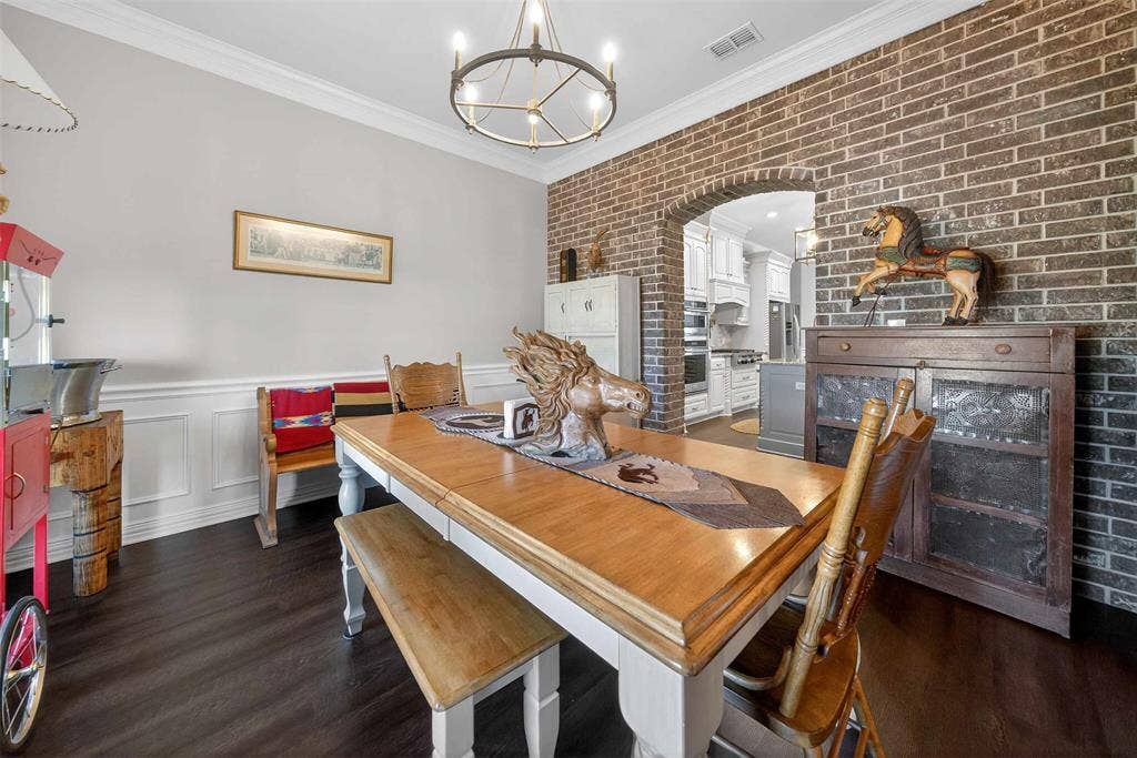 23151 Champion Drive, Lindale, TX 75771 Dining area featuring brick wall, a chandelier, crown molding, wainscoting, and dark wood finished floors