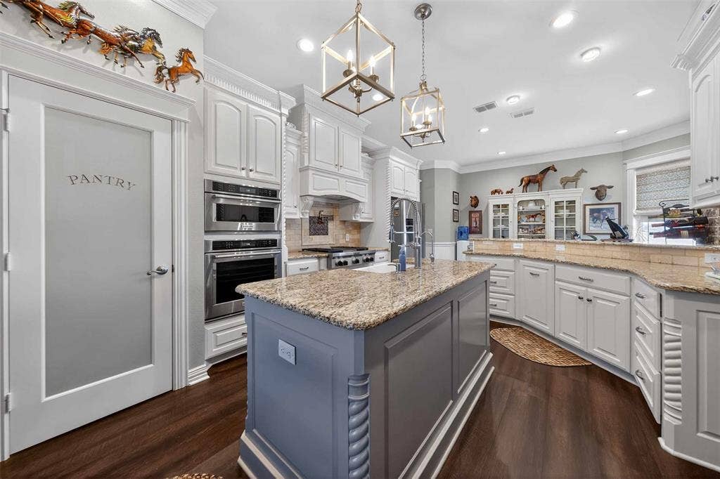 23151 Champion Drive, Lindale, TX 75771 Kitchen with light stone countertops, ornamental molding, dark wood-type flooring, a kitchen island with sink, and suspended lighting