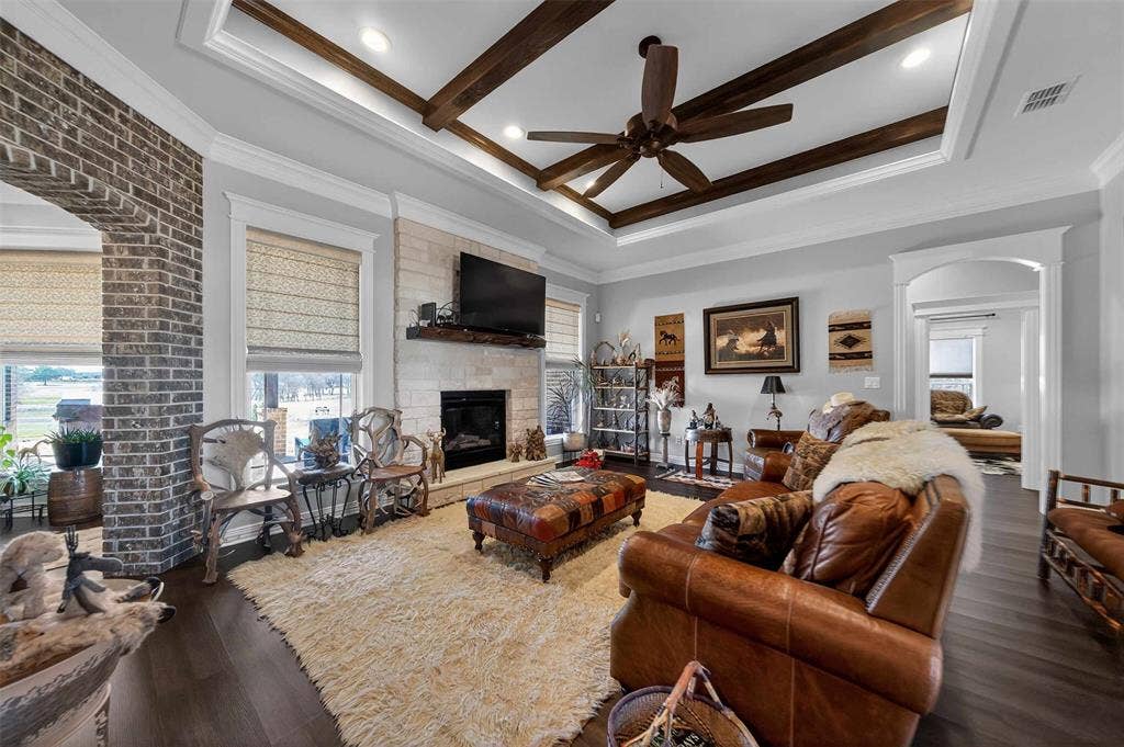 23151 Champion Drive, Lindale, TX 75771 Living room with a stone fireplace, a ceiling fan, dark wood-type flooring, ornamental molding, and arched walkways