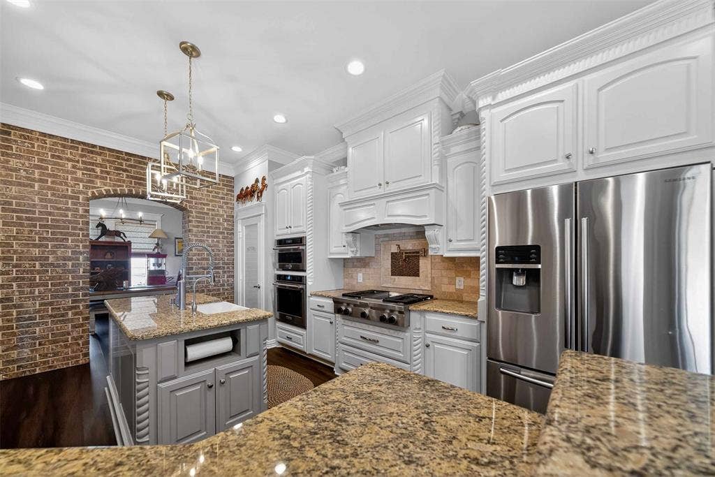 23151 Champion Drive, Lindale, TX 75771 Kitchen with brick wall, stainless steel appliances, light stone countertops, white cabinets, and crown molding