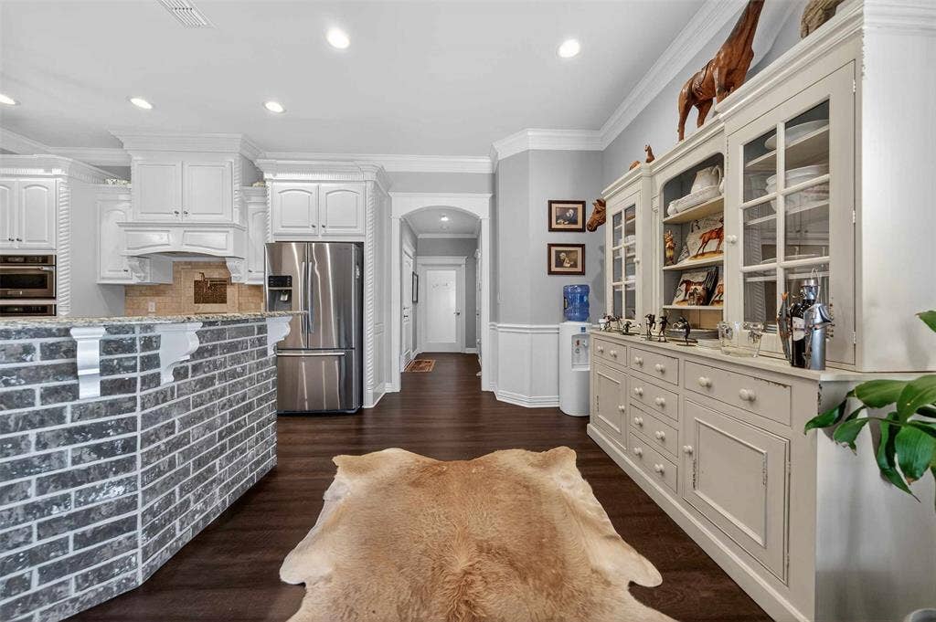 23151 Champion Drive, Lindale, TX 75771 Kitchen with arched walkways, crown molding, glass fronted cabinets, stainless steel appliances, and a wainscoted wall