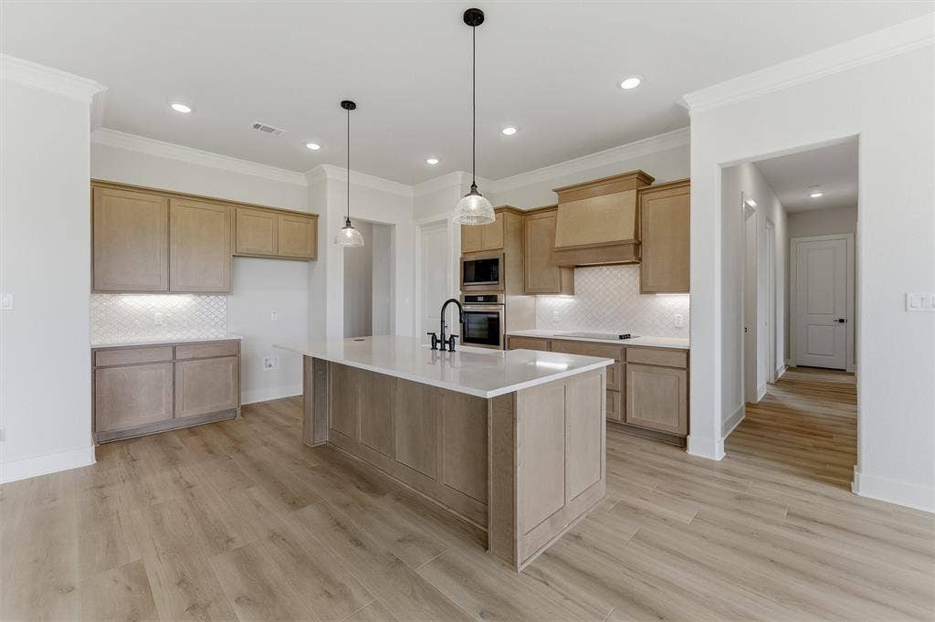 2204 Continent Court, Krum, TX 76249 Spacious kitchen featuring a large central island with a white solid surface countertop, light wood-finish cabinetry, built-in double ovens, and a white geometric tile backsplash