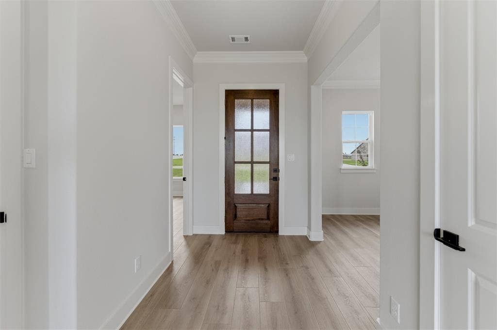 2204 Continent Court, Krum, TX 76249 Entryway featuring a dark wood door with frosted glass panes, light wood-finish flooring, white baseboards, crown molding, and light gray wall paint