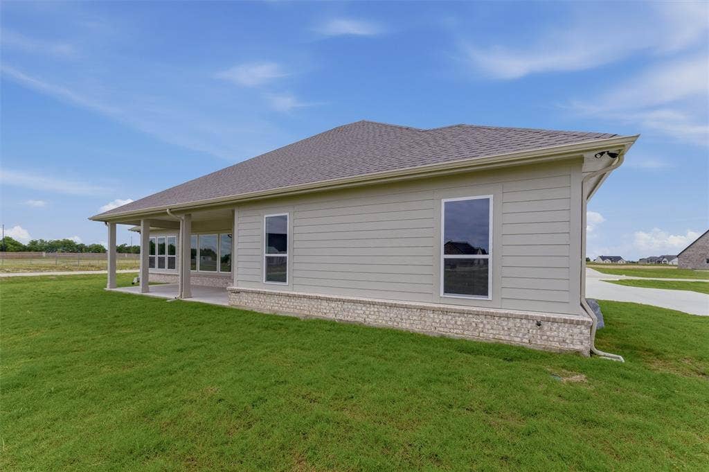 2204 Continent Court, Krum, TX 76249 Rear exterior showcasing an expansive covered patio, a stone and brick foundation, light-colored horizontal siding, and a shingle roof