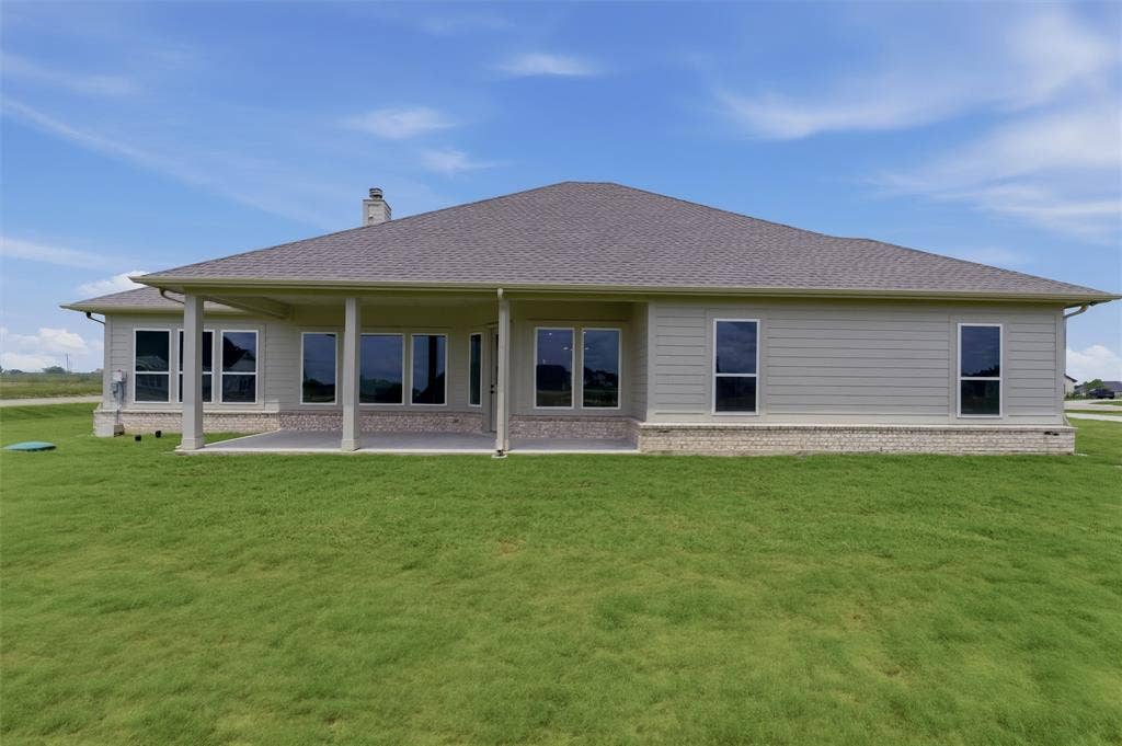 2204 Continent Court, Krum, TX 76249 Rear exterior featuring a covered patio, multiple large windows, light-colored siding, a stone-accented foundation, and a shingled roof