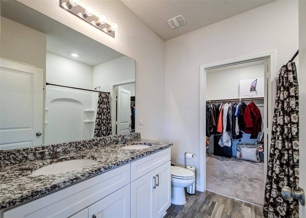 Bathroom featuring a walk in closet, double vanity, a shower with shower curtain, and dark wood-style floors