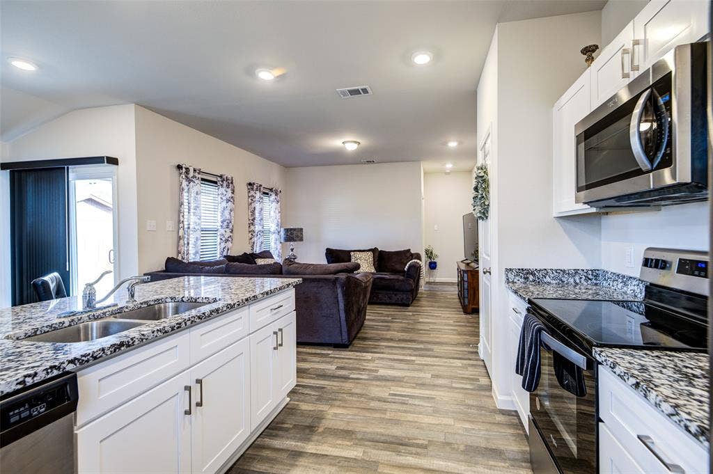 Kitchen with stainless steel appliances, white cabinets, dark stone counters, and recessed lighting