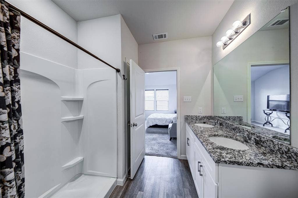 Bathroom featuring double vanity, ensuite bath, dark wood-type flooring, and curtained shower