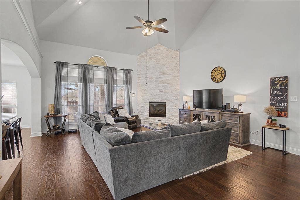 3409 Florence Drive, Corinth, TX 76210 Living area with dark wood finished floors, a floor to ceiling stone fireplace, a ceiling fan, arched walkways, and vaulted ceiling