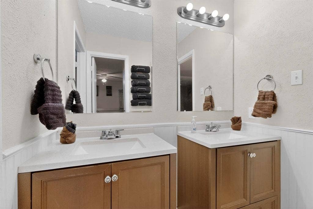 2315 Blue Sage Lane, Arlington, TX 76014 Full bathroom featuring a wainscoted wall, a textured wall, two vanities, and a decorative wall