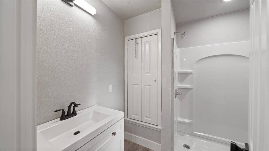 129 King Arthur Road, Mabank, TX 75156 This bathroom features a vanity with a white sink and dark-toned faucet, a light fixture above the vanity, and a shower with built-in shelving