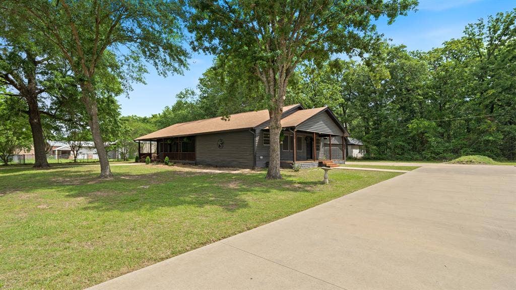 129 King Arthur Road, Mabank, TX 75156 The property features a dark-colored exterior with a front porch, a well-maintained lawn with mature trees, and a concrete driveway