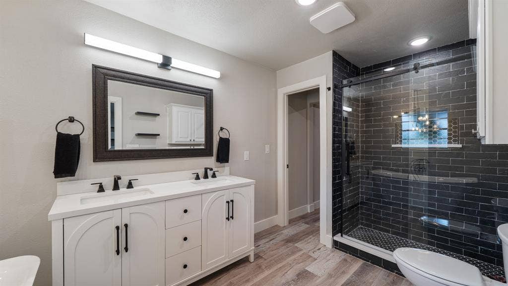 129 King Arthur Road, Mabank, TX 75156 Bathroom featuring a double vanity with white cabinetry, a glass-enclosed shower with dark subway tiles, and wood-look flooring
