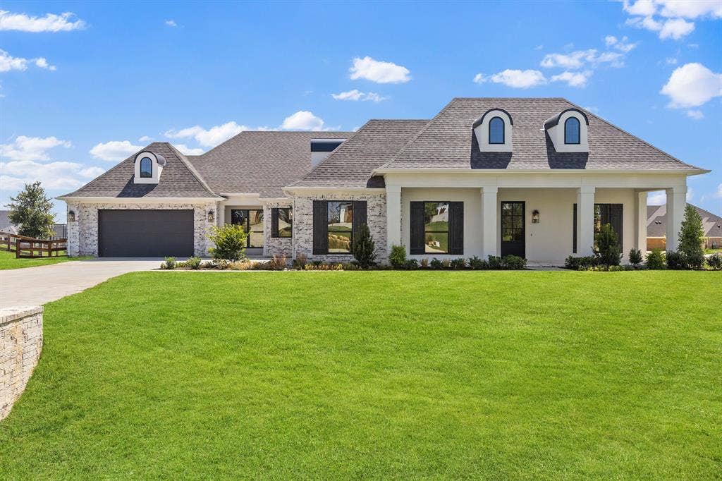 3333 Bridgegate Avenue, Northlake, TX 76247 Exterior featuring a combination of brick and stucco finishes, covered front porch with substantial columns, a dark shingle roof, arched dormer windows, and an integrated garage with a dark panel door